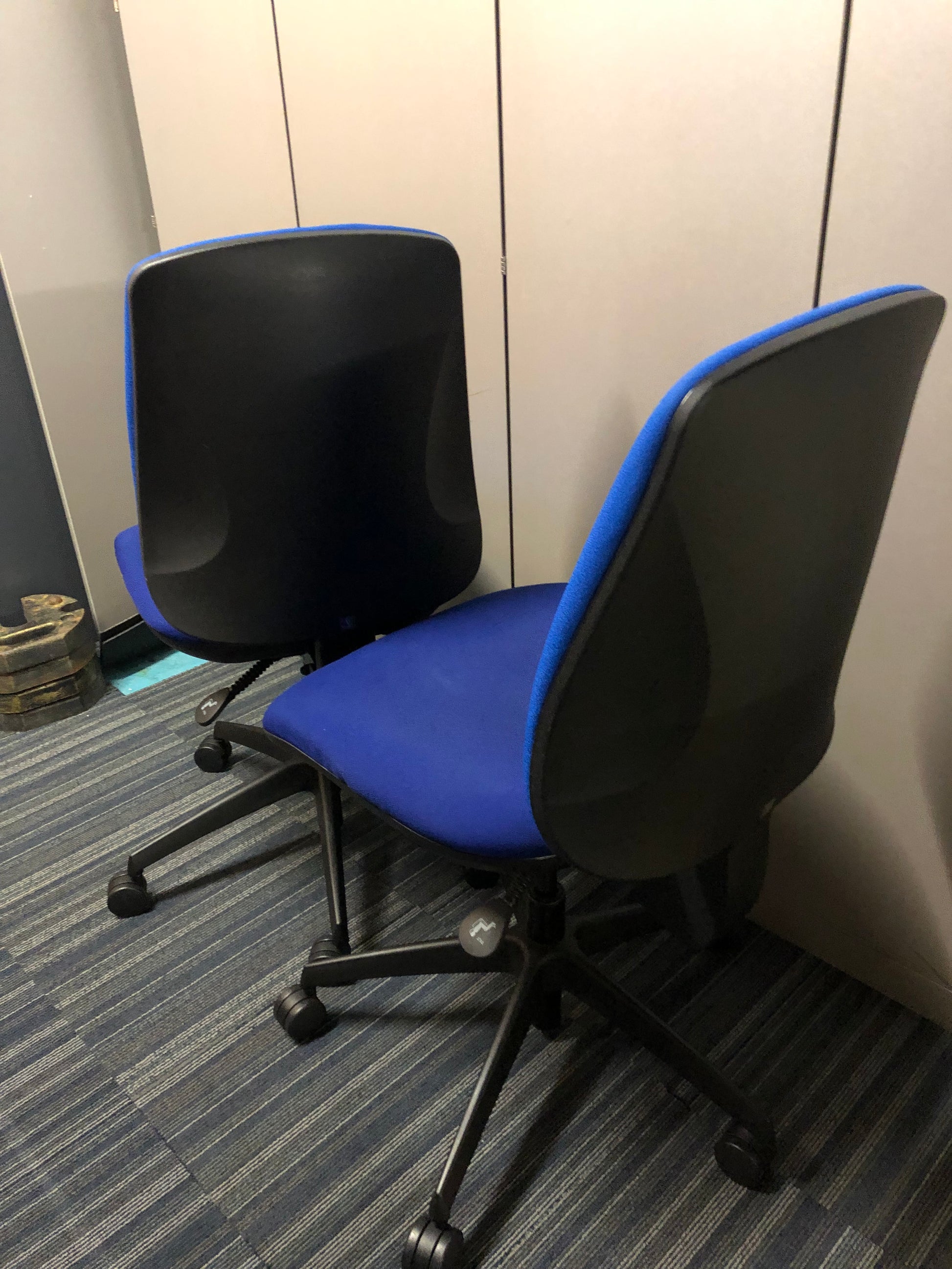The black backs of 2 blue office computer swivel chairs