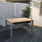 Clear office workstation table with grey legs, in front of a tall green plant