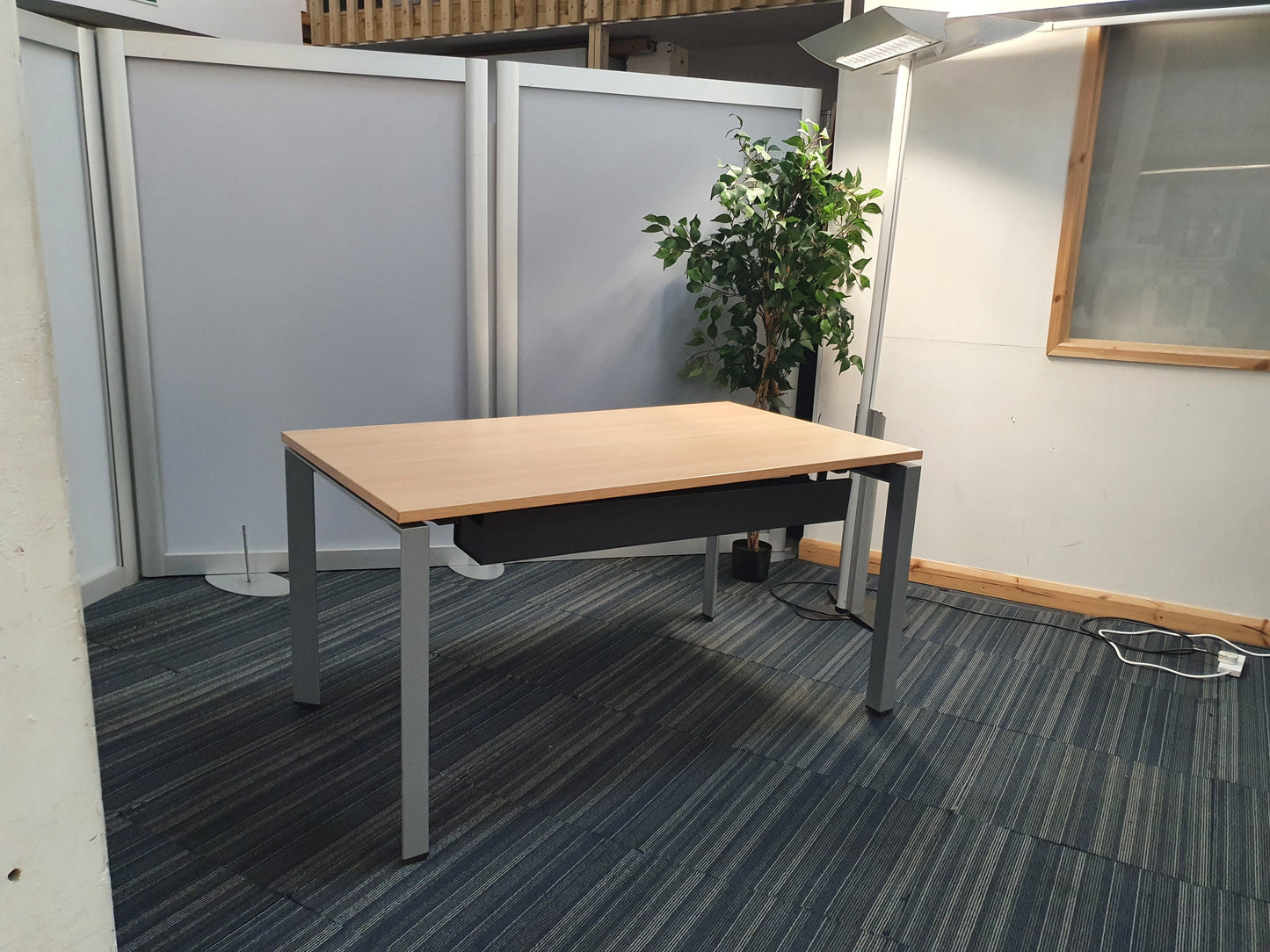 Clear office workstation table with grey legs, in front of a tall green plant