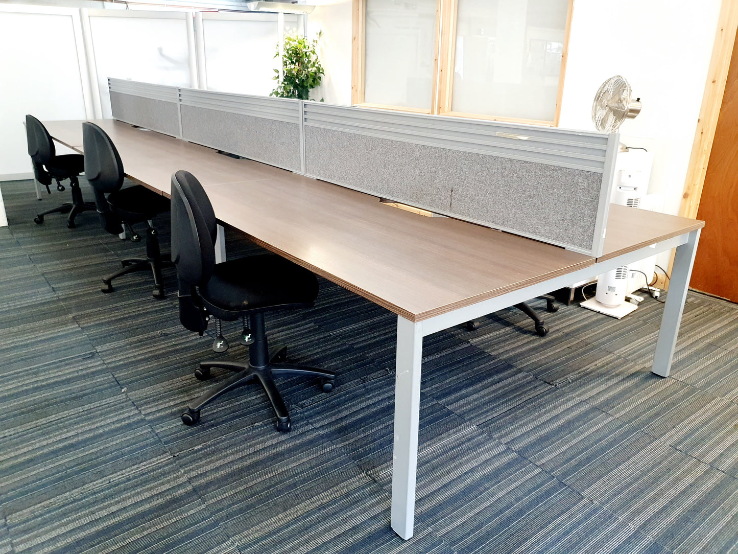 black wheelie chairs tucked under walnut office pod desk with grey dividers