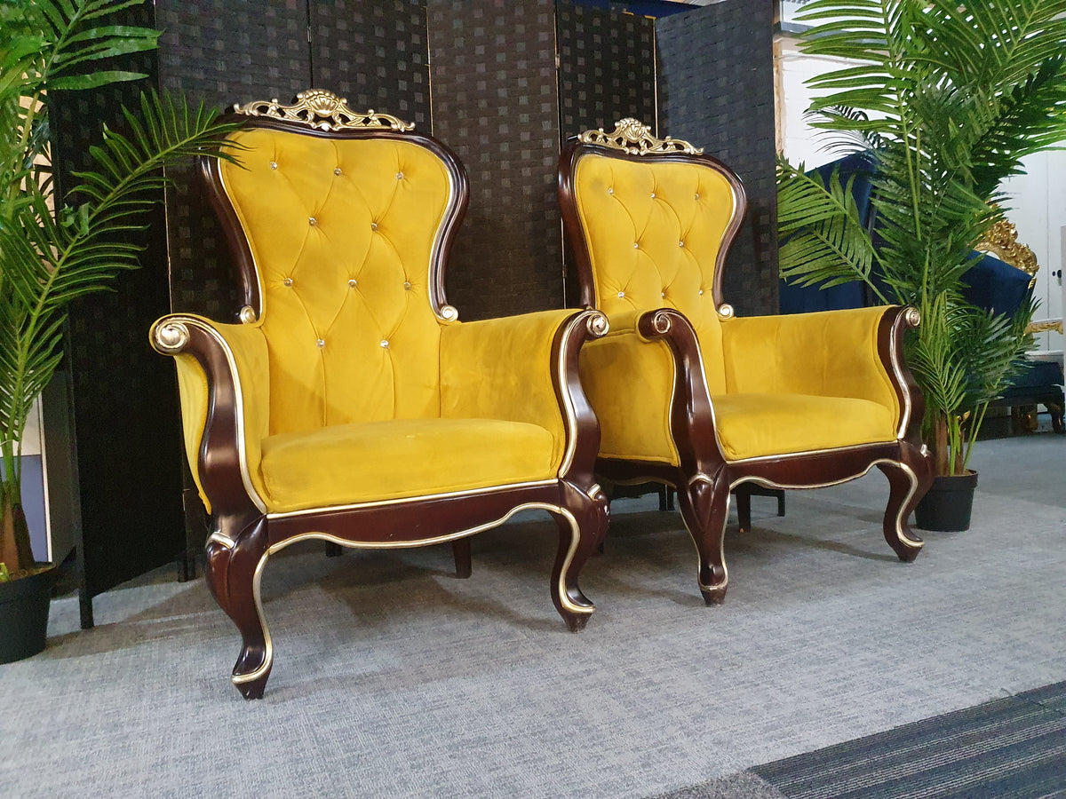 Two antique upholstered armchairs with yellow upholstery and wooden high backs, carved with intricate patterns.
