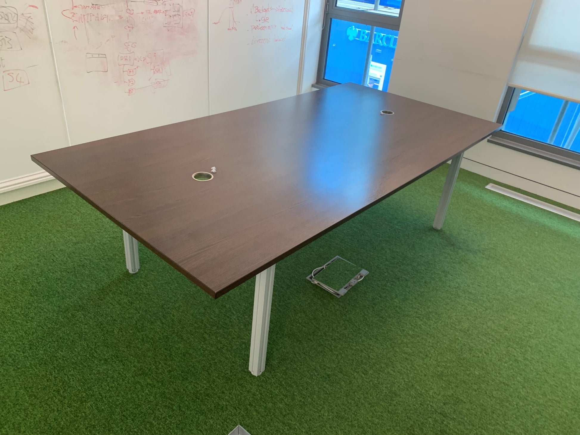 Walnut conference table on green carpet in room with large windows