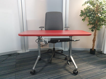 Red table in front of grey computer chair, right, tall plant in green#