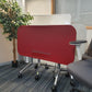 Left, tall green plant, centre, folded red office table, right, grey swivel chair