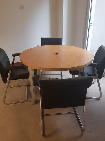 Round wooden table with four black chairs in a room with white walls and a window.