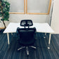 Study table with black mesh chair tucked in, green plant to its left and white folded tables to its right