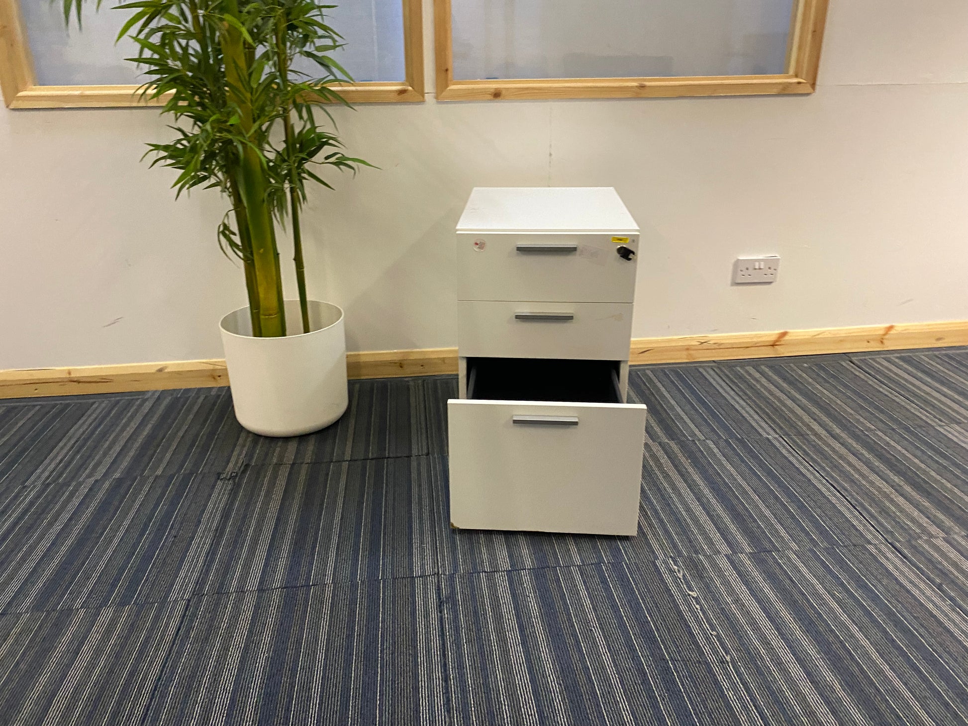 three drawer cabinet with open bottom drawer and tall green plant