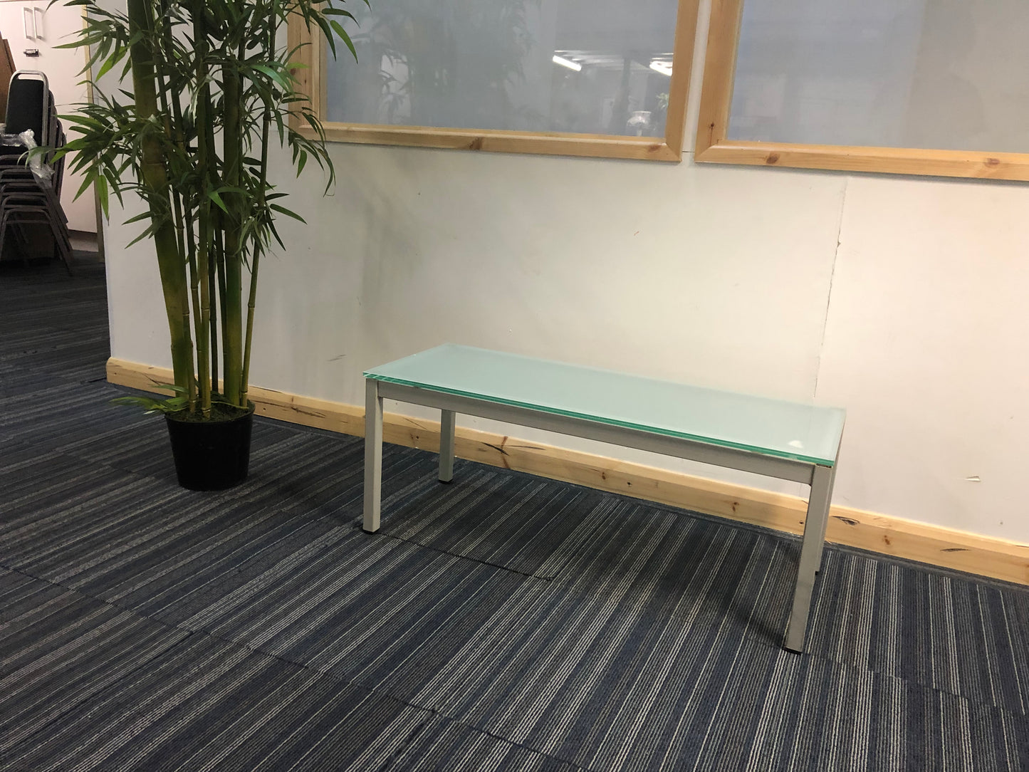 centre, blue glass reception coffee table tall green plant, top left, stacked chairs