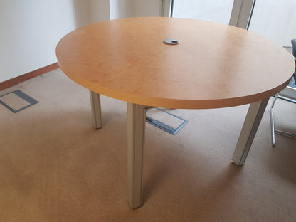 Round wooden table with metal legs in a room with light-colored floor and white walls.