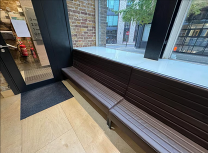 A chocolate brown office reception strip settee against a wall, with a glass door in the background.