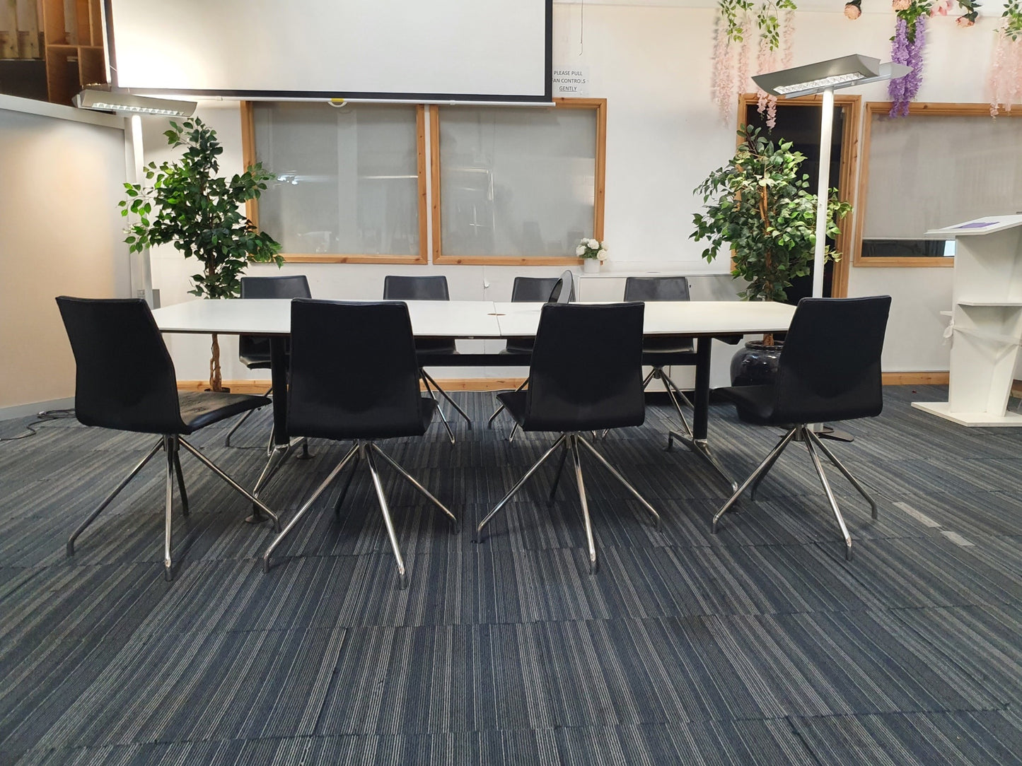 white boardroom table, 2 green plants, 8 meeting chairs