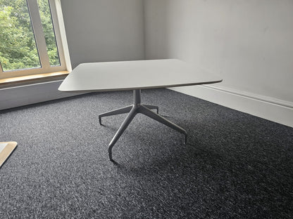A white square coffee table with a chrome base located in an interior setting, possibly an office or home environment.