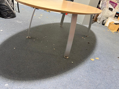 Secondhand maple-coloured boardroom table features a distinctive oval shape supported by four silver legs.