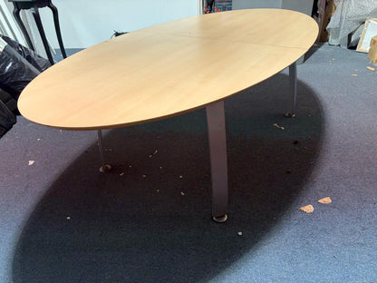 Secondhand maple-coloured boardroom table features a distinctive oval shape supported by four silver legs.