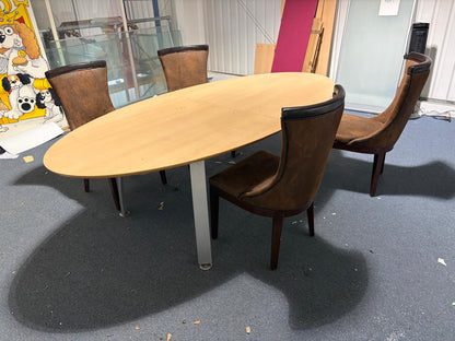 Secondhand maple-coloured boardroom table features a distinctive oval shape supported by four silver legs.