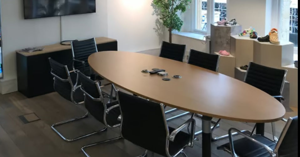 Modern conference room with oval table and chairs, TV on wall, and plant.