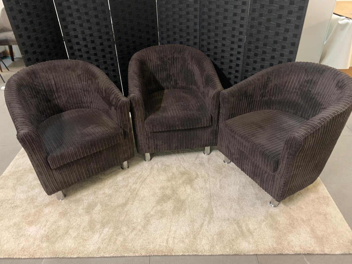 Three brown upholstered tub on a light rug with a dark textured wall in the background.