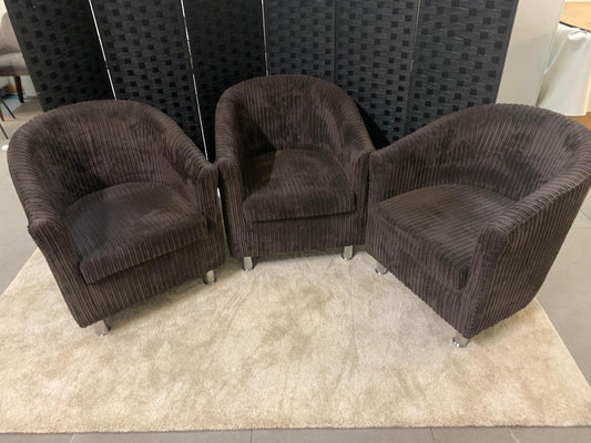 Three brown upholstered tub on a light rug with a dark textured wall in the background.