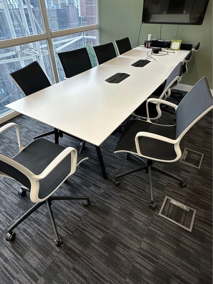 Modern conference room with a long white table and black chairs in an office setting.