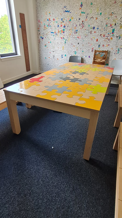 Partial view of a room with a colorful puzzle table, a window, and a wall with children's drawings.