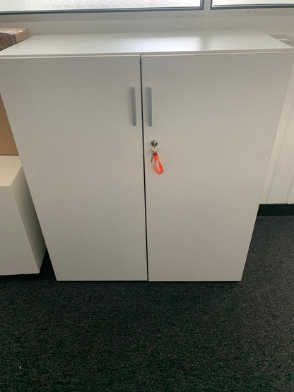A white two-door storage cabinet with slim silver handles and a key with an orange loop, set against a dark gray carpeted floor.