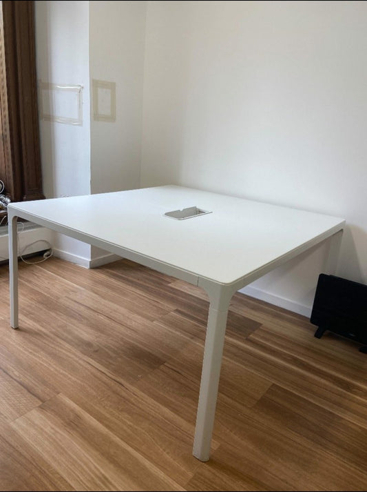 White office table in a room with wooden flooring and a white wall.