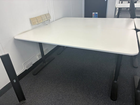 A white rectangular meeting table with black metal legs, shown in an office or classroom setting with gray carpet and a white wall.